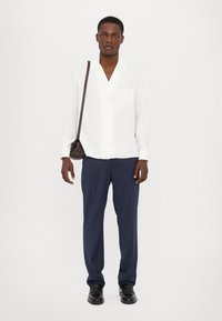 Cămașă albă cu mâneci lungi, cu nasturi și un singur buzunar pe piept, asociată cu pantaloni negri eleganți și pantofi negri. Geantă maro tip crossbody.