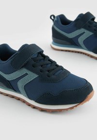 Marina sneakers med nät- och mockamaterial, med kardborreband, snördesign och en texturerad gummisula med bruna detaljer.