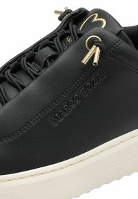 Baskets en cuir noir avec une finition texturée, des accents dorés, un logo et une semelle en caoutchouc blanche. Design à lacets avec des détails matériels uniques.