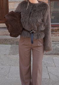 Jachetă maro din blană artificială, cu un croi scurt și mâneci lungi, asortată cu pantaloni maro cu talie înaltă, cu o textură subtilă și tiv evazat. Ține o geantă maro închis din piele intoarsă.