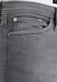 Jeans de mezclilla gris con un diseño estándar de cinco bolsillos, que cuentan con herrajes metálicos y una tela texturizada, mostrando detalles de costura y un ligero desgaste.