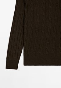 Dark brown knitted sweater with a cable pattern, featuring a round neckline and a button detail at the shoulder. Soft texture.