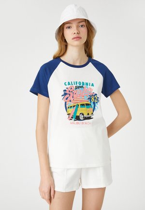 Vit t-shirt med marinblå raglanärmar, med en färgglad grafik av "California Surfer 82" som visar en vintage skåpbil och palmträd.