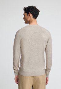 Helles beige gestricktes Sweatshirt mit rundem Ausschnitt, langen Ärmeln und geripptem Saum. Glatte Textur mit einem dezenten Muster.