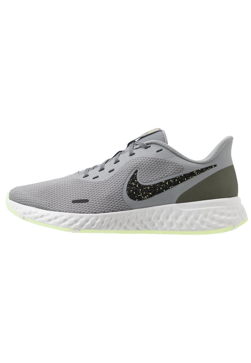 Chaussure de running Nike gris clair avec un swoosh noir à pois, semelle texturée blanche et accent de talon vert olive, vue de côté sur fond blanc.