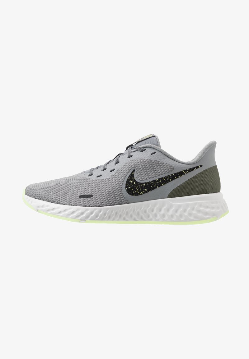 Chaussure de running Nike gris clair avec un swoosh noir à pois, semelle texturée blanche et accent de talon vert olive, vue de côté sur fond blanc.