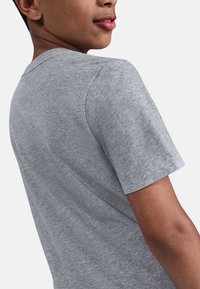 Camiseta de algodón gris con mangas cortas, cuello redondo y una textura suave. Costuras visibles a lo largo de la costura del hombro y los bordes de las mangas.