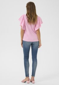 Rožnata kratkotrajna majica s naborki, kombinirana z oprijetimi modrimi kavbojkami in svetlo rožnatimi petkami. Gladek material in sproščen kroj.