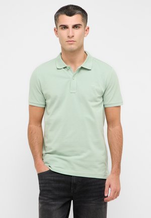 Hellgrünes Polohemd, kurze Ärmel, geknöpfter Kragen, weicher Baumwollstoff, mit einem kleinen Logo auf der Brust, getragen mit dunklen Jeans.