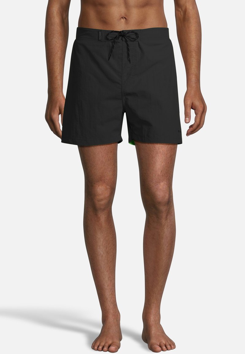 Zwarte zwembroek met een rijgband in de taille, van een effen kleur en lichtgewicht stof. Opvallende groene accenten zijn zichtbaar langs de zoom.