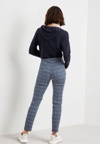 Sweat-shirt à capuche bleu marine et pantalon ajusté avec un motif floral blanc. Le pantalon présente une taille haute et des jambes fuselées. Porté avec des baskets blanches.
