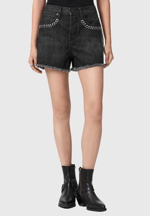 Sorte denimshorts med sølvnitter langs lommerne og frynset kant, båret med sorte ankelstøvler og en sort top.