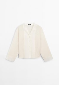 Blouse courte à boutons en blanc cassé, avec un tissu texturé sur les manches et les côtés, et un devant et un col lisses.
