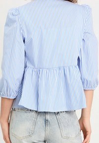 Haut peplum rayé bleu et blanc avec manches bouffantes, confectionné dans un tissu léger ; le dos présente une ceinture froncée.