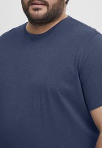 Tamsiai mėlynas trumpomis rankovėmis marškinėliai, pagaminti iš medvilnės ir sintetinių pluoštų mišinio. Turi apvalų iškirpimą ir lygų, vientisą tekstūrą be matomų raštų.