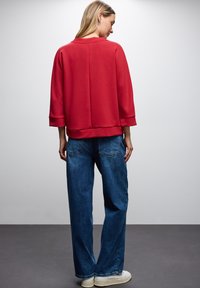 Top corto rosso con colletto rotondo e taglio dritto, abbinato a jeans a gamba larga blu e sneakers bianche. Tessuto dalla texture liscia.