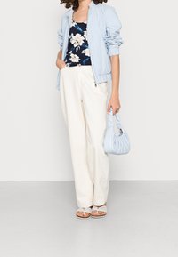 Světle modrá bomber bunda přes květinový námořnický top, doplněná bílými širokými kalhotami, světle modrou kabelkou a šedými sandály s pruhy na prstech.