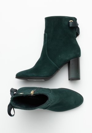 Bottines en daim vert foncé à talons carrés, fermeture éclair latérale et bande noire décorative à l'arrière.