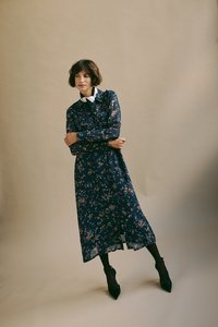 Nawojenny sukienka w kwiaty z kołnierzykiem i długimi rękawami. Lekki, przezroczysty materiał w wielokolorowe wzory kwiatowe. Czarne szpiczaste szpilki.