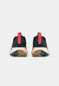 Black and green athletic shoes featuring a textured upper, prominent red pull tab, and a durable brown rubber outsole with a multi-directional tread pattern.
