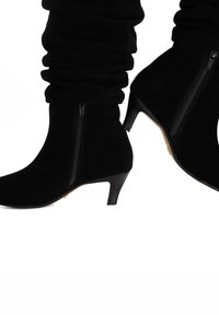 Black suede ankle boots with slouchy upper, pointed toe, and 3-inch heel. Features a side zipper for easy wear. Texture is soft and smooth.