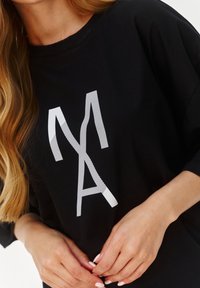Czarny, oversize t-shirt z białym, skośnym napisem z literą "A" na przodzie. Miękka tkanina o luźnym kroju.