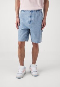 Svetlomodré denim šortky s voľným strihom, so bočnými vreckami a roztrhnutým lemom. V kombinácii s bielymi teniskami, ktoré majú farebné akcenty.