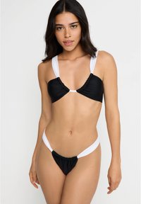 Biquíni preto e branco com um design franzido, alças grossas e parte de baixo de corte alto. O material aparenta ser suave com um leve brilho.