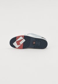 Sneaker sole with mixed materials; black rubber with hexagonal patterns, red and white accent sections, flat and textured for grip.