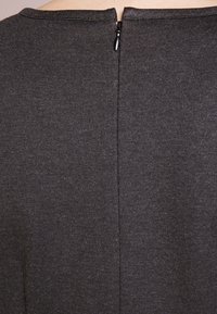 Mörkgrå klädesplagg med en slät textur, med en dragkedja på baksidan och en enkel, rundad halsringning. Minimalistisk design utan mönster eller accentuerande detaljer.