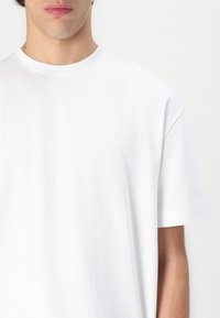 Valkoinen puuvillat-paita, jossa on pyöreä kaula-aukko ja lyhyet hihat, pehmeällä ja sileällä kunnolla. Ei näkyviä kuvioita tai malleja.