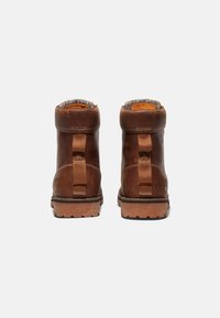 Botas de cuero marrón hasta el tobillo con un acabado texturizado, que presentan pestañas laterales y una suela de goma robusta, vistas desde la parte posterior.
