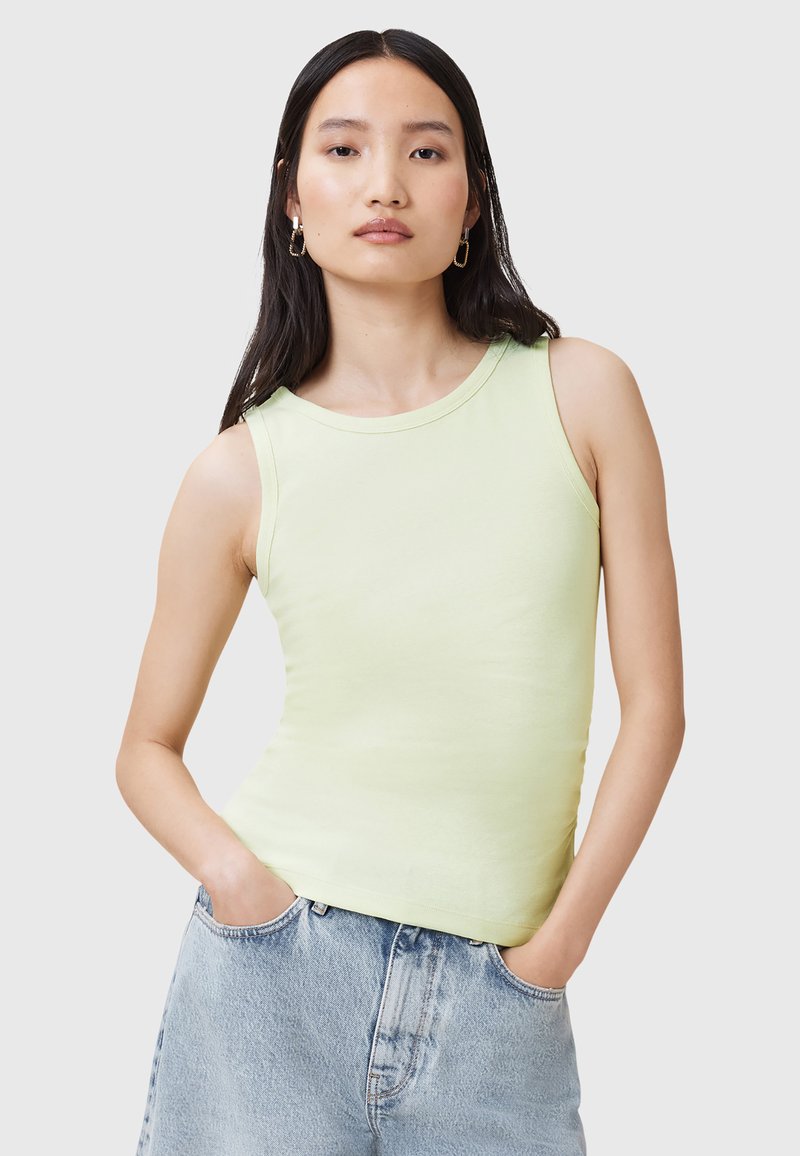 Top sin mangas de color verde claro en un estilo ajustado, fabricado con un material suave de textura lisa y escote redondeado. Presentado con pantalones cortos de denim.
