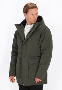 Jachetă căptușită de culoare verde măslin, cu glug�ă detașabilă, fermoar frontal, două buzunare laterale și căptușeală interioară texturată. Prezintă închideri cu capse și fermoar.