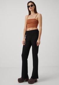 Orange crop top with wavy black pattern; black elastic waist pants; brown clogs with holes; dark sunglasses; smooth textures.