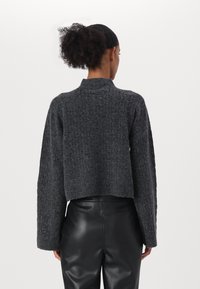 Maglione lavorato a maglia grigio scuro, accollato e con maniche ampie, abbinato a pantaloni di pelle nera con una finitura texturizzata.