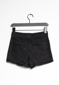 Pantalones cortos de mezclilla negra con un ajuste relajado, que cuentan con dos bolsillos traseros y costuras visibles. Se cuelgan en un perchero de metal negro contra un fondo blanco.