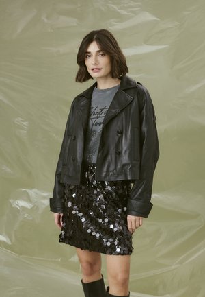 Giacca cropped in pelle nera con bottoni doppi, t-shirt grafica grigia sotto, e una minigonna nera in paillettes con paillettes circolari.