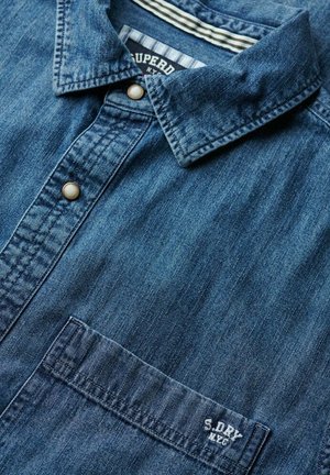 Denim shirt in donkerblauw, met een button-down kraag, een voorzak en geborduurde branding. Zachte textuur met een lichte vervaging.