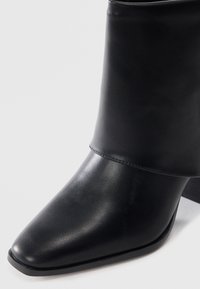 Black ankle boot with a pointed toe and textured finish. Features a folded cuff and a low, chunky heel. Made of synthetic material.