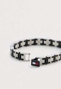 Czarna i srebrna bransoletka z połączonymi metalowymi sekcjami oraz zapięciem z detalem logo, łącząca gładkie i fakturowane powierzchnie.