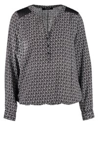 Blouse à manches longues présentant un motif noir et blanc, avec un décolleté en V et des accents en cuir noir sur les épaules.