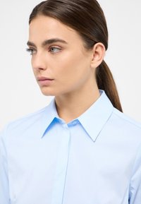 Light blue collared shirt made of smooth fabric, featuring a button placket and sharp collar, with a fitted design and no visible patterns.