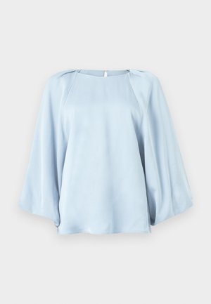 Blouse bleu clair avec de larges manches longues fluides et un col rond, fabriquée en tissu lisse et soyeux.