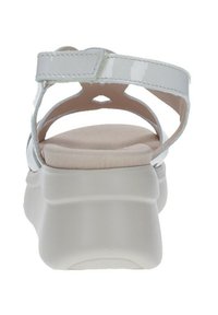 Sandalias de charol blancas con una planta acolchada de color beige, tira ajustable y una suela gruesa blanca con fondo texturizado.