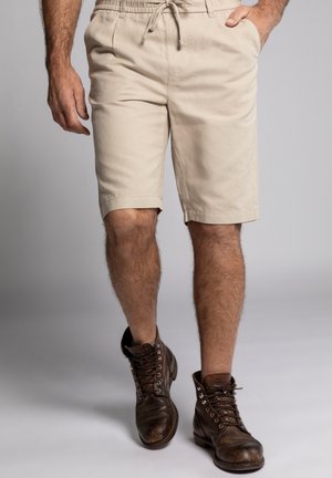 Beige Baumwollshorts mit einem elastischen Bund und Kordelzug, ausgestattet mit Seitentaschen. Getragen mit braunen Leder-Schnürstiefeln.