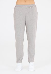 Hellegraue Jogginghosen aus weichem Stoff mit elastischem Bund, seitlichen Taschen und schmalem Beinansatz. Getragen mit weißen Sneakers.