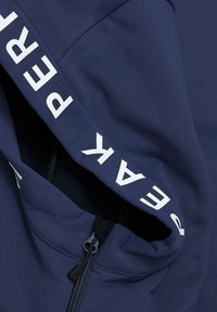 Mørkeblå jakke lavet af blødt stof, der har en lynlås og dristig hvid tekst langs ærmet. Glat tekstur med et strømlinet design.