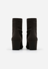 Bruna ankle boots gjorda av mjukt tyg, med en slouchad design och en kraftig klack för ökad stabilitet. Bakifrån syns sömmen utan anslutningar.