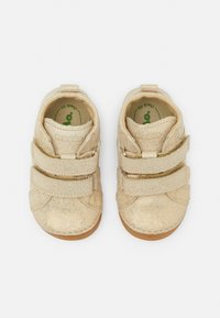 Gouden glittersneakers met twee klittenbandsluitingen. Rondneus, zacht materiaal en lichtbruine rubberen zool. Het interieur heeft een label voor controle van de pasvorm.